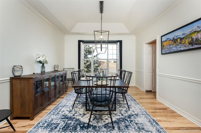 dining space featuring ornamental molding, a tray ceiling, light wood finished floors, and baseboards