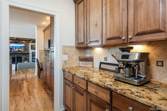 kitchen with light wood finished floors, brown cabinetry, light stone counters, a fireplace, and backsplash