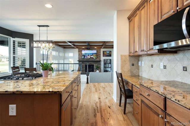 kitchen featuring brown cabinets, stainless steel appliances, light wood-style flooring, decorative backsplash, and a stone fireplace