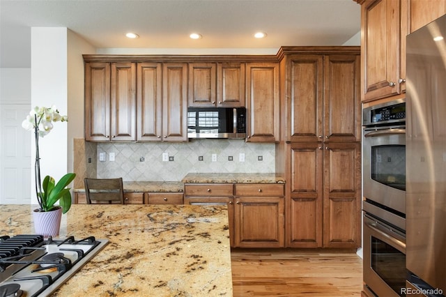 kitchen featuring appliances with stainless steel finishes, light stone counters, and brown cabinets