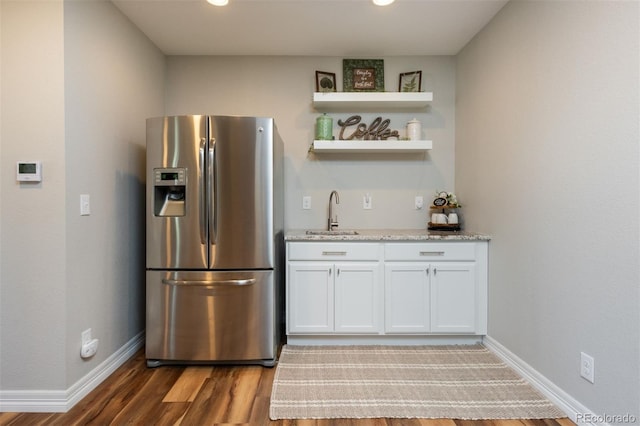 kitchen with light stone counters, wood finished floors, white cabinetry, stainless steel refrigerator with ice dispenser, and a sink