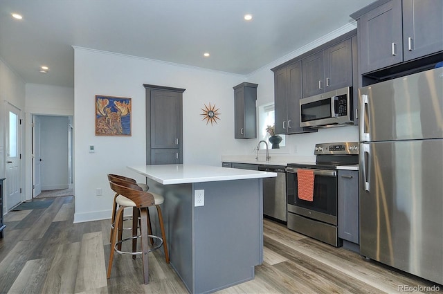 kitchen with appliances with stainless steel finishes, crown molding, sink, hardwood / wood-style flooring, and a center island