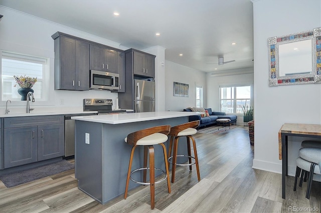 kitchen with a kitchen bar, light wood-type flooring, stainless steel appliances, sink, and a center island