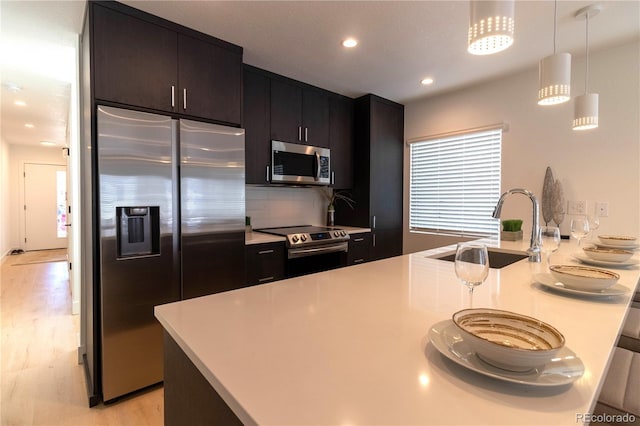 kitchen featuring sink, appliances with stainless steel finishes, hanging light fixtures, decorative backsplash, and light wood-type flooring