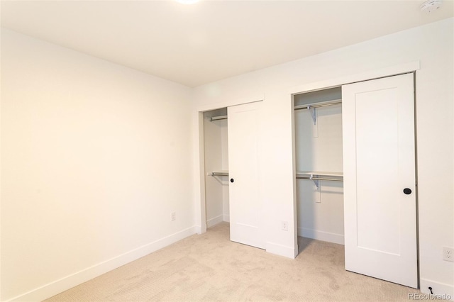 unfurnished bedroom featuring multiple closets and light carpet