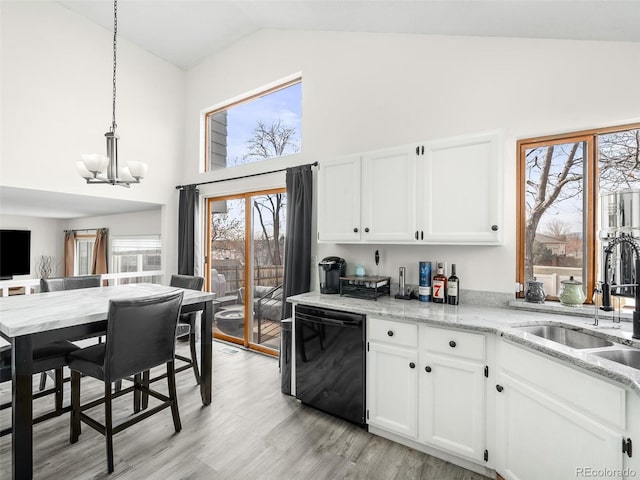 kitchen with light wood finished floors, dishwasher, light stone counters, white cabinetry, and a notable chandelier