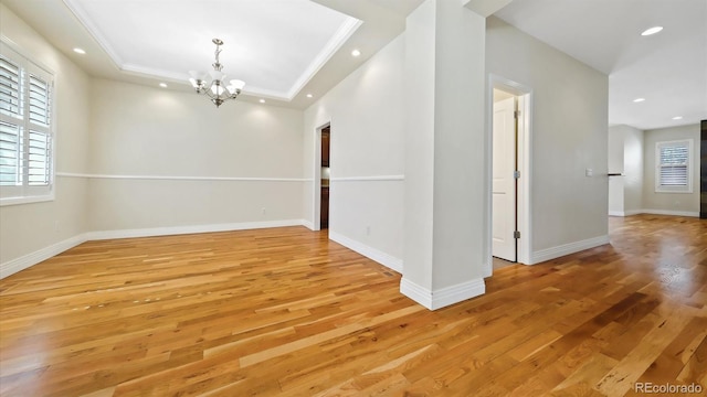 unfurnished room with ornamental molding, a raised ceiling, light hardwood / wood-style floors, and a notable chandelier