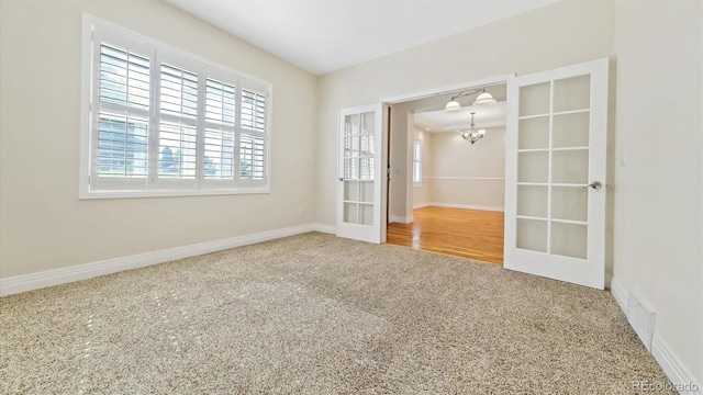 empty room featuring french doors, a chandelier, and carpet