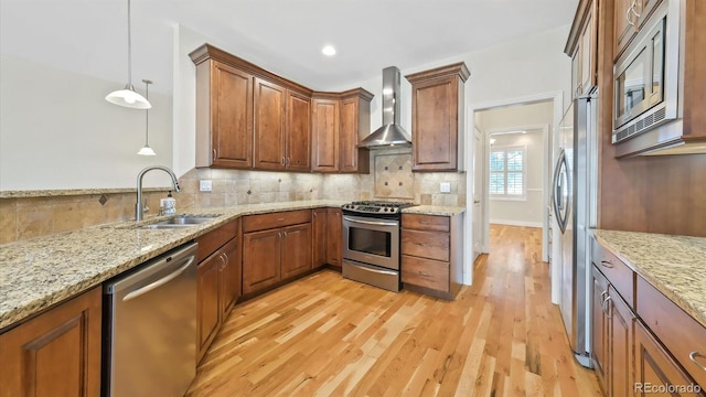 kitchen featuring wall chimney exhaust hood, sink, light stone counters, appliances with stainless steel finishes, and pendant lighting