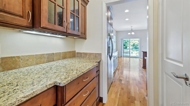 kitchen with light stone countertops, hanging light fixtures, and light hardwood / wood-style flooring