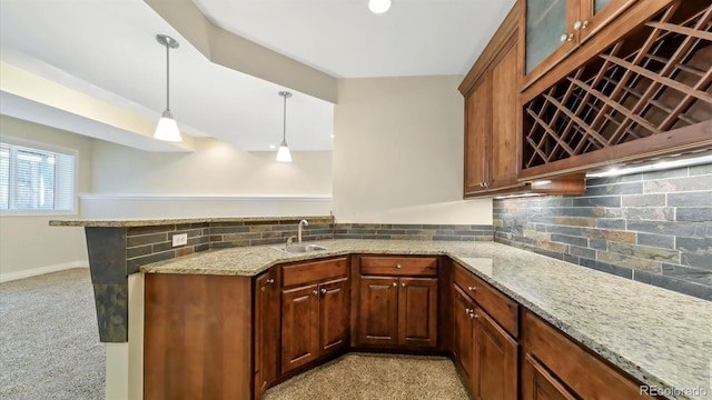 kitchen featuring pendant lighting, sink, light stone counters, tasteful backsplash, and kitchen peninsula