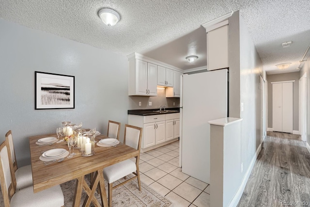 kitchen with a textured ceiling, light tile patterned floors, baseboards, and white cabinets