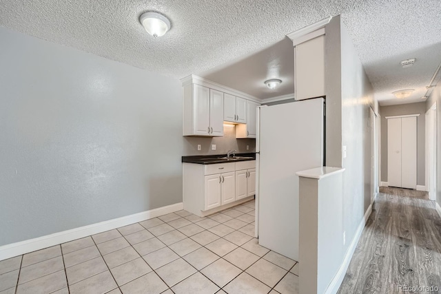 kitchen with a textured ceiling, dark countertops, white cabinetry, and baseboards