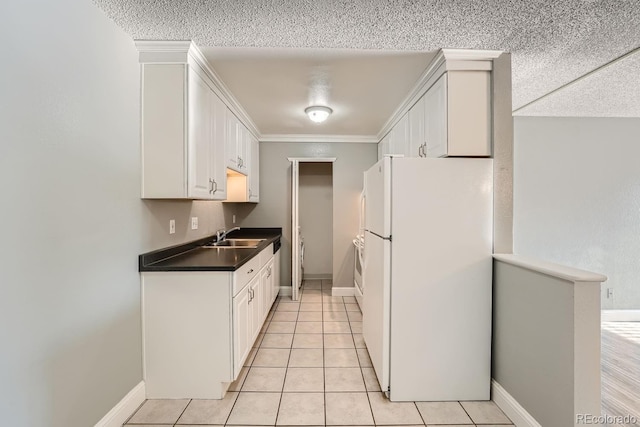 kitchen featuring light tile patterned floors, white cabinets, dark countertops, freestanding refrigerator, and a sink