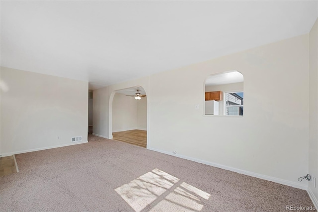 empty room with arched walkways, baseboards, visible vents, and light colored carpet