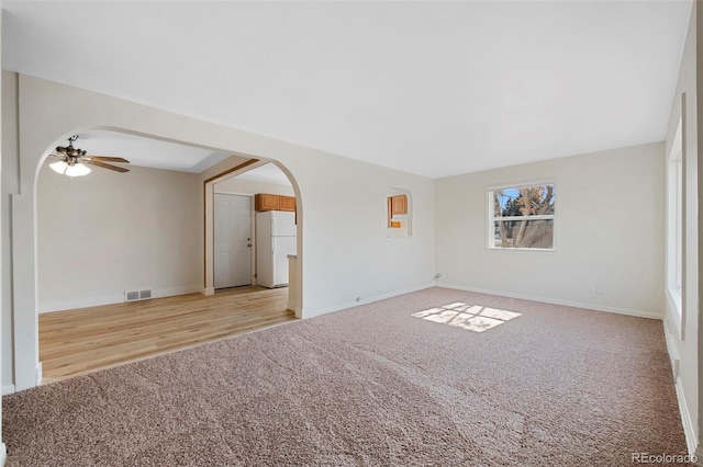 spare room with arched walkways, carpet, visible vents, a ceiling fan, and baseboards