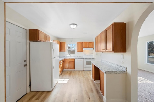 kitchen featuring white appliances, light countertops, light wood-type flooring, under cabinet range hood, and a sink