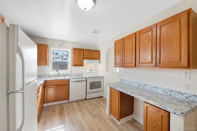 kitchen featuring white appliances, under cabinet range hood, brown cabinets, and a sink