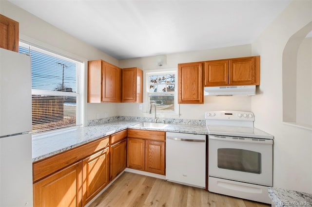 kitchen featuring arched walkways, under cabinet range hood, white appliances, a sink, and light wood finished floors