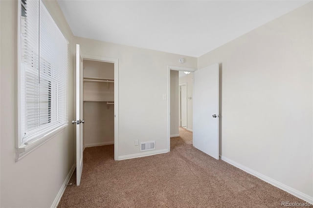 unfurnished bedroom featuring carpet floors, baseboards, visible vents, and a walk in closet