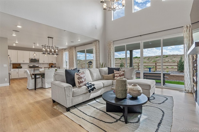 living room with a towering ceiling, light hardwood / wood-style flooring, and a chandelier