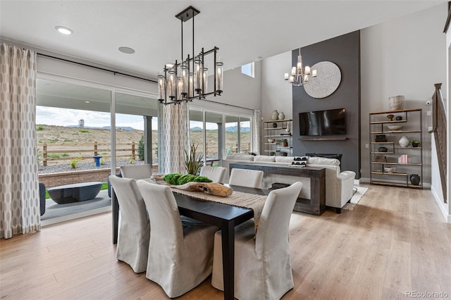 dining space with a towering ceiling, a notable chandelier, and light hardwood / wood-style flooring