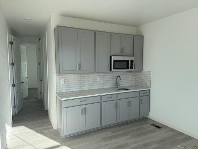 kitchen featuring stainless steel microwave, gray cabinets, light wood-type flooring, and a sink