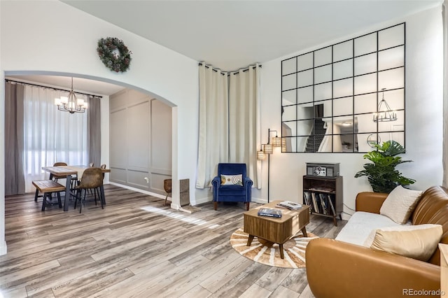 living room featuring arched walkways, light wood-type flooring, and an inviting chandelier