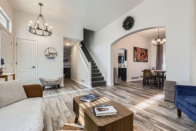 living area with arched walkways, a notable chandelier, light wood-type flooring, and visible vents