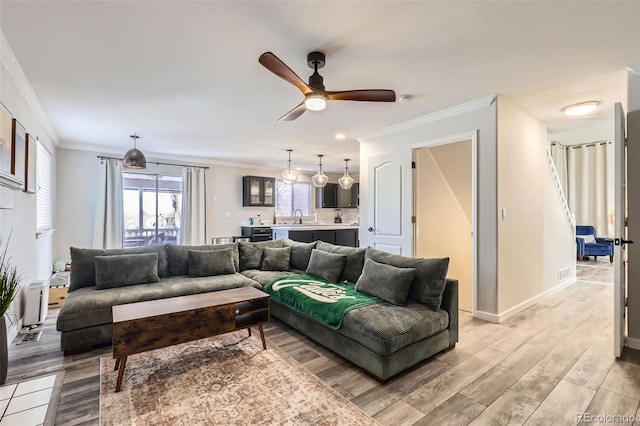 living area with a ceiling fan, baseboards, visible vents, ornamental molding, and light wood-style floors