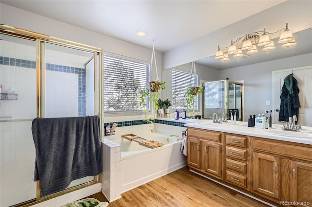 bathroom with double vanity, a stall shower, wood finished floors, a bath, and a sink