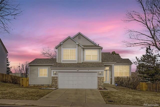 traditional-style home featuring a garage, stone siding, concrete driveway, and fence