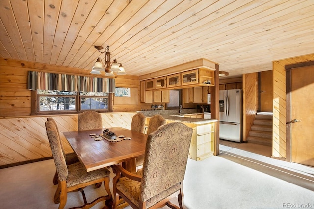 dining space with a notable chandelier, light colored carpet, wooden ceiling, and wooden walls