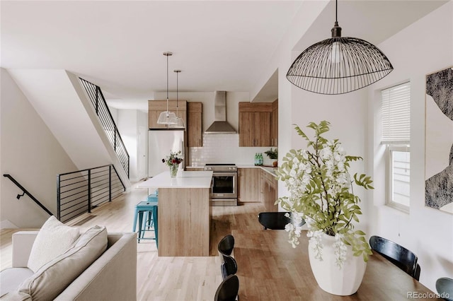 interior space featuring wall chimney exhaust hood, pendant lighting, stainless steel stove, a center island, and light hardwood / wood-style flooring