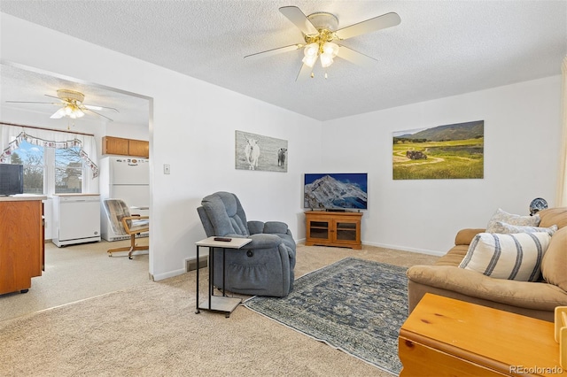 living room with ceiling fan, baseboards, a textured ceiling, and light colored carpet