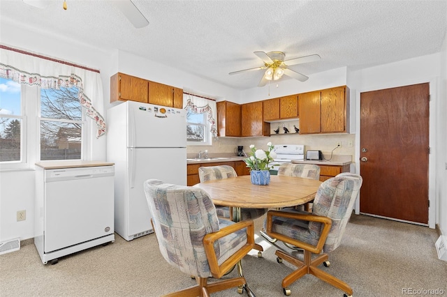 kitchen with light countertops, visible vents, brown cabinetry, a ceiling fan, and white appliances