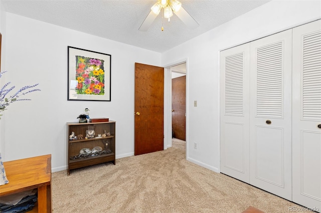 bedroom featuring a closet, light carpet, ceiling fan, a textured ceiling, and baseboards