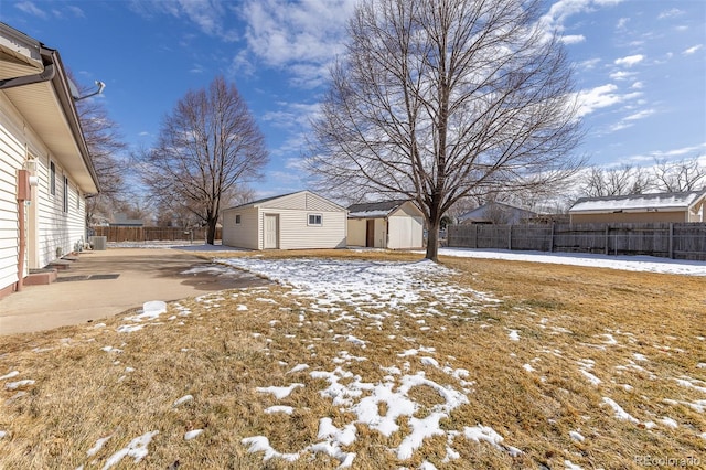 snowy yard featuring a storage shed, a fenced backyard, and an outdoor structure