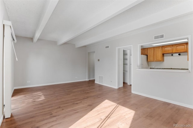 unfurnished living room featuring light wood-type flooring, baseboards, visible vents, and beam ceiling