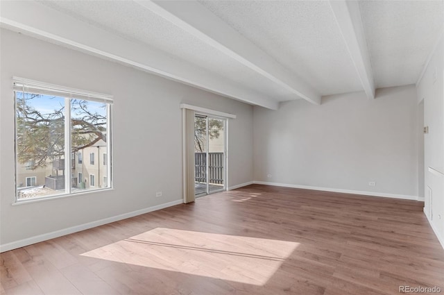 unfurnished room featuring a healthy amount of sunlight, a textured ceiling, wood finished floors, and beamed ceiling