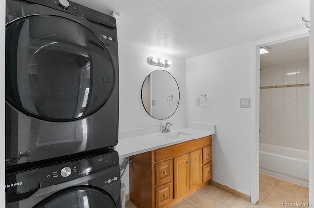 washroom with light tile patterned floors, stacked washer / dryer, a textured ceiling, laundry area, and a sink