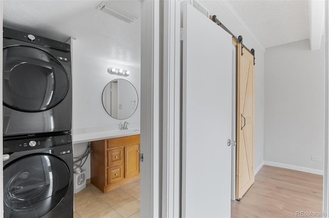 clothes washing area with stacked washer / dryer, laundry area, a sink, a textured ceiling, and a barn door