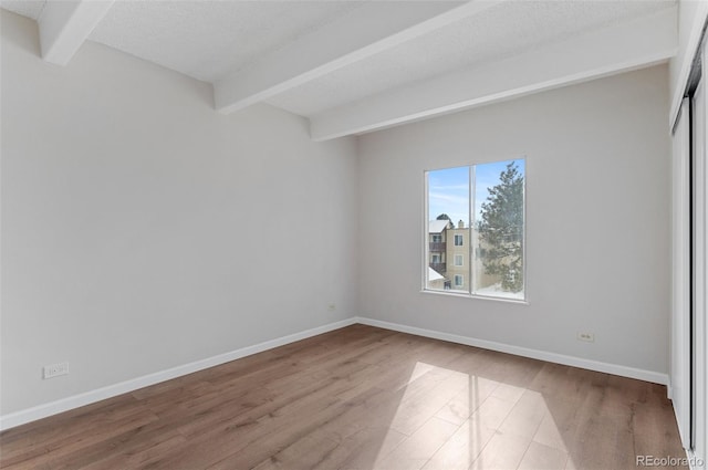 spare room with baseboards, beamed ceiling, and wood finished floors