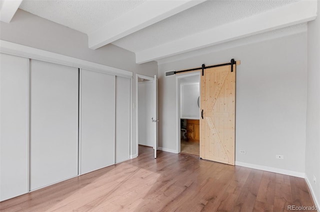 unfurnished bedroom featuring a barn door, light wood-type flooring, visible vents, beam ceiling, and a textured ceiling