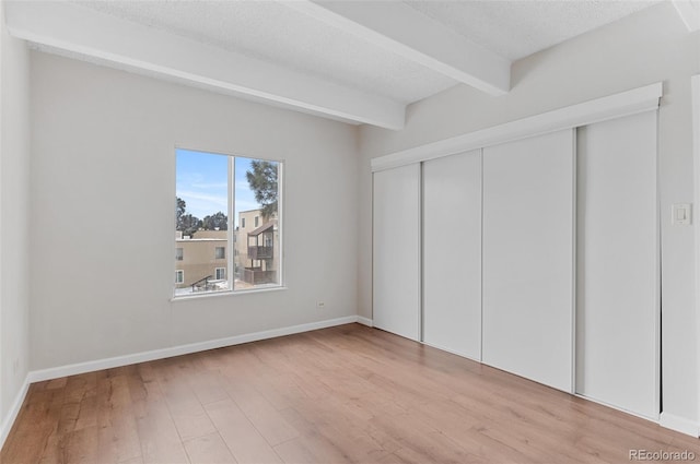 unfurnished bedroom featuring light wood-type flooring, a closet, beamed ceiling, and a textured ceiling