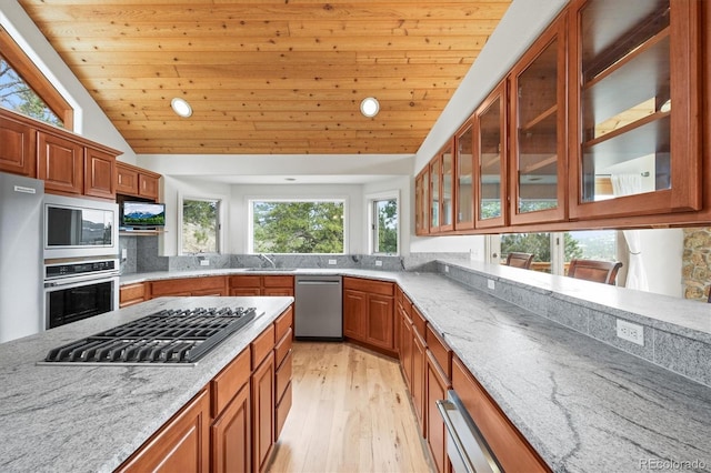 kitchen featuring light stone countertops, light wood-style floors, appliances with stainless steel finishes, and brown cabinets