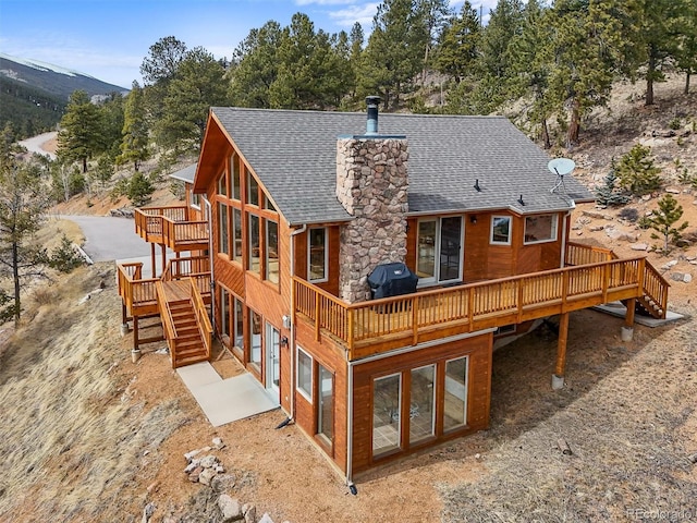 back of house featuring stairs, a deck, a chimney, and a shingled roof