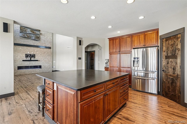 19423 W 52nd Dr, Golden, CO 80403 - kitchen with light wood-style flooring, dark countertops, arched walkways, stainless steel fridge with ice dispenser, and a center island