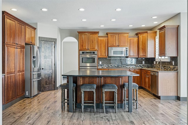 19423 W 52nd Dr, Golden, CO 80403 - kitchen featuring stainless steel appliances, a breakfast bar, decorative backsplash, a kitchen island, and light wood-style flooring