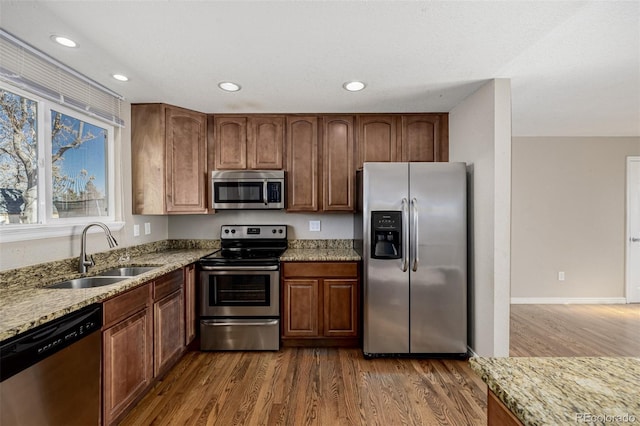 kitchen with a sink, stainless steel appliances, light stone countertops, and dark wood-style floors